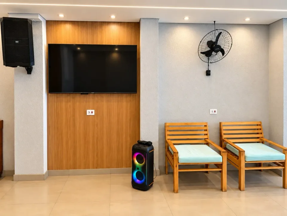 TV na parede, caixas de som e poltronas no espaço do karaokê